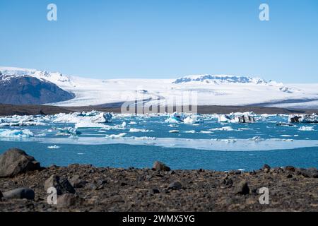 Eaux bleues glacées avec glace fondante flottante et collines enneigées sur le rivage en Islande Banque D'Images