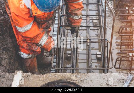 Un travailleur utilise du fil de liage en acier pour attacher des tiges d'acier aux barres de renfort en gros plan. Structures en béton armé - fabrication d'une cage d'armature en acier f Banque D'Images