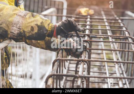 Un travailleur utilise du fil de liage en acier pour attacher des tiges d'acier aux barres de renfort en gros plan. Structures en béton armé - fabrication d'une cage d'armature en acier f Banque D'Images