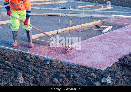 Constructeurs coulant et nivelant du béton prêt à l'emploi humide dans le coffrage lors de la construction d'un nouveau sentier Banque D'Images