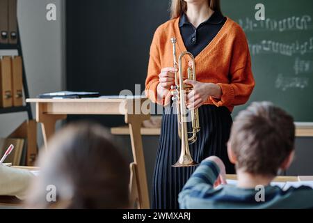Photo de recadrage à mise au point sélective d'une enseignante de musique méconnaissable tenant un instrument en laiton debout devant des enfants en classe Banque D'Images