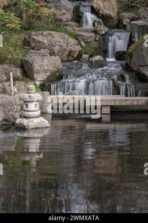 Cascade longue exposition cascade lisse soyeuse sur les falaises rocheuses dans le jardin de Kyoto. Lanterne décorative japonaise en pierre devant avec érable orange Banque D'Images