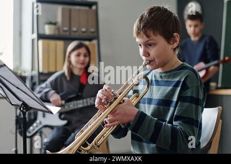 Plan de mise au point sélective d'un garçon caucasien pratiquant la trompette dans un orchestre scolaire moderne, espace copie Banque D'Images