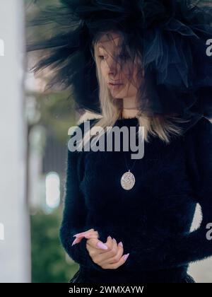 Pensive jeune blonde caucasienne mince femme pâle regardant, son visage encadré par un grand chapeau de tulle noir Banque D'Images