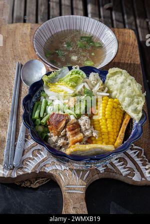 Nouilles bâtonnets de riz garnies de porc haché, porc croustillant, wontons frits, maïs sucré, tofu frit, chou chinois, haricots longs Yard, germe de haricots, Goji Be Banque D'Images