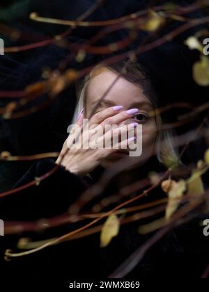 Le visage d'une femme est partiellement couvert par sa main et ses branches d'automne, créant un sentiment de mystère Banque D'Images