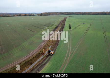 Photographie par drone de fossé de drainage de nettoyage de pelle hydraulique dans un champ agricole pendant le matin nuageux d'automne Banque D'Images