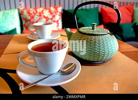 Les deux tasses et une théière de thé rooibos sur une table à côté d'un canapé avec des oreillers colorés, à Ponta Delgada, Açores Banque D'Images