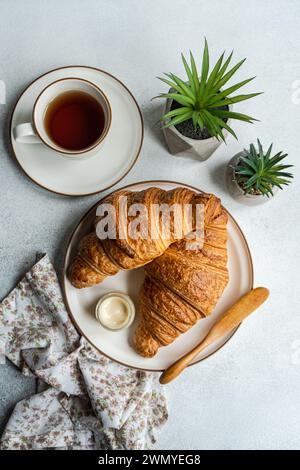 Vue de dessus d'une scène de petit déjeuner avec des croissants feuilletés, un pot de miel, une tasse de thé et des succulentes décoratives en pot sur une surface texturée Banque D'Images