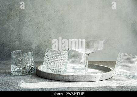 Un arrangement artistique de verres texturés vides sur un plateau rond en pierre, projetant des ombres douces sous la lumière ambiante Banque D'Images