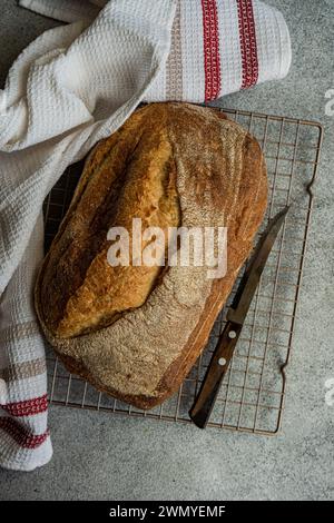 Vue de dessus de pain de levain de seigle fraîchement cuit est assis sur une grille métallique, accompagné d'un couteau à pain et d'un chiffon blanc avec des rayures rouges Banque D'Images