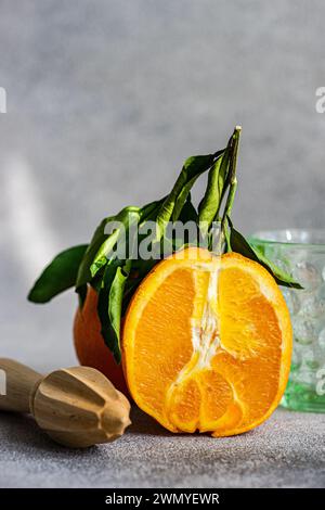 Une orange éclatante et fraîche coupée avec des feuilles vertes à côté d'une centrifugeuse en bois sur un fond neutre Banque D'Images