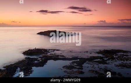 Ciel serein au crépuscule projetant des couleurs pastel douces sur un océan tranquille avec une petite île et un rivage rocheux à Gran Canaria Banque D'Images