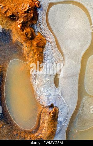 Vue aérienne des configurations de glace avec biofilm et sédiments de couleur rouille dans un étang gelé Banque D'Images