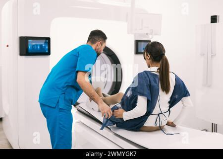 Un professionnel de la santé dans les gommages aide une patiente sur un appareil IRM, se préparant à l'imagerie diagnostique dans un cadre clinique. Banque D'Images
