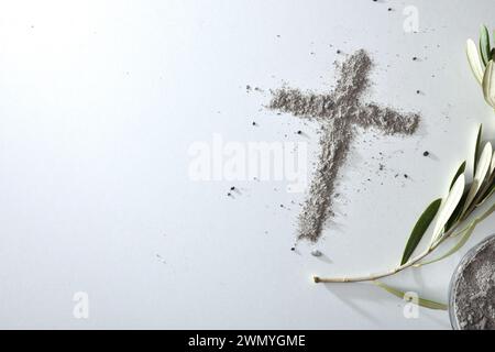 Croix faite avec des cendres sur une table blanche avec des feuilles d'olivier et un récipient plein de cendres. Vue de dessus. Banque D'Images