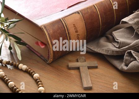 Bible antique sur table en bois avec croix chrétienne en bois, feuilles d'olivier et tissu brun. Vue surélevée. Banque D'Images