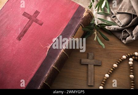 Bible antique sur table en bois avec croix, feuilles d'olivier et tissu. Vue de dessus. Banque D'Images