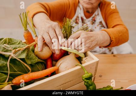 Personne âgée organisant une variété de légumes fraîchement récoltés dans une boîte en bois sur une table Banque D'Images