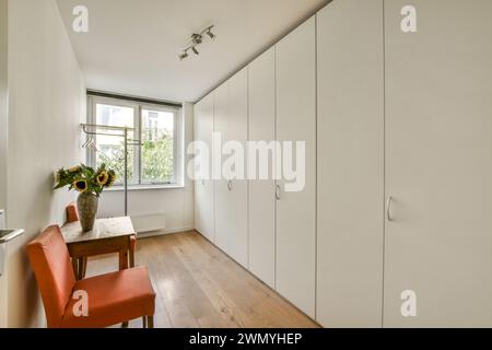 Une chambre minimaliste lumineuse avec une grande armoire intégrée, parquet et un petit bureau avec un vase de tournesols, avec beaucoup de lueur naturelle Banque D'Images