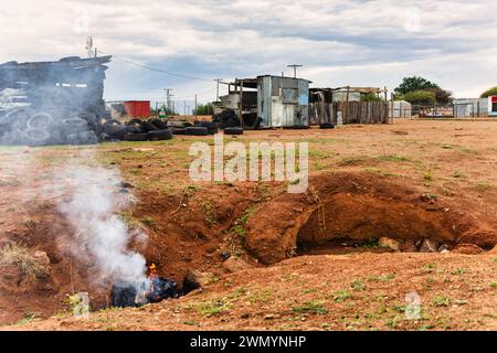 village informel en afrique près d'une colline, cabane faite de fer ondulé et de bois, sacs poubelle brûlant au premier plan Banque D'Images