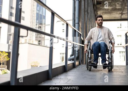 Jeune homme barbu aux cheveux foncés sur un fauteuil roulant Banque D'Images