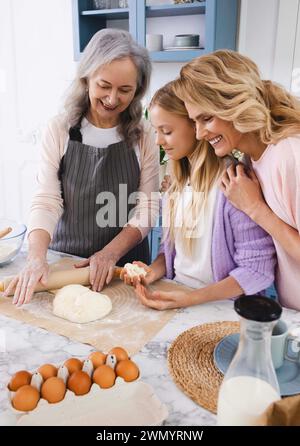 Heureuse adolescente enfant ont plaisir à rouler la pâte pour les biscuits avec sa grand-mère et sa mère, préparant de délicieux biscuits ensemble dans la cuisine Banque D'Images