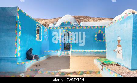 Assouan, Egypte - Une femme vêtue de vêtements traditionnels est assise devant une maison nubienne colorée à Assouan, Egypte Banque D'Images