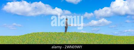 Solitude dans la sérénité : homme en costume debout seul sur une colline verte luxuriante sous ciel bleu Banque D'Images