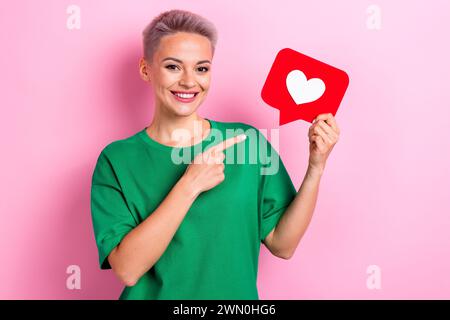 Portrait de sourire dentelé de fille joyeuse indiquer la tenue de bras de doigt comme l'icône de notification espace vide isolé sur fond de couleur rose Banque D'Images