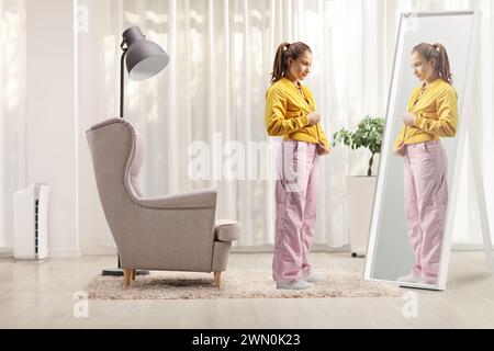 Photo pleine longueur d'une adolescente zippant sa veste devant un miroir à la maison Banque D'Images