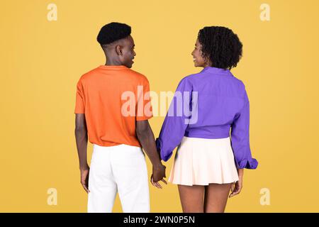 Vue arrière d'un jeune couple tenant la main, avec l'homme dans une chemise orange Banque D'Images