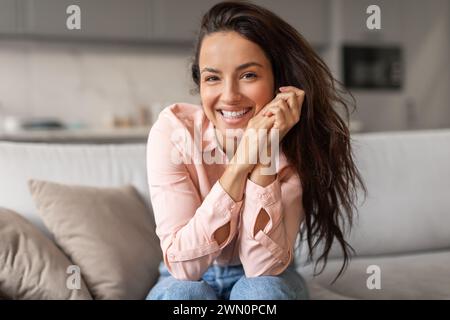 Femme aux yeux brillants avec un sourire joyeux assis sur le canapé Banque D'Images