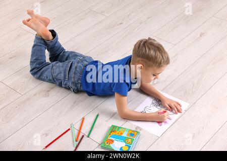 Mignon petit garçon dessinant sur le sol chaud à la maison. Système de chauffage Banque D'Images