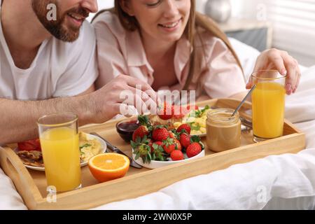 Couple heureux mangeant un petit déjeuner savoureux au lit, gros plan Banque D'Images