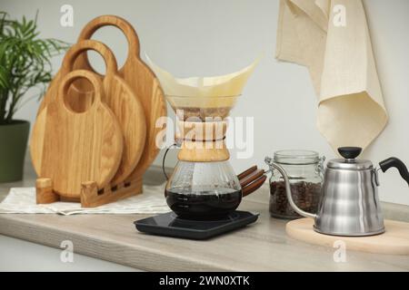 Préparation de café goutte à goutte. Cafetière chemex en verre avec filtre en papier, pot de haricots et bouilloire sur comptoir en bois dans la cuisine Banque D'Images