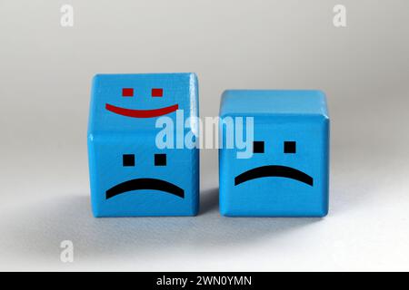 Cubes bleu clair avec des visages tristes et heureux sur fond gris clair Banque D'Images