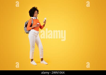 Jeune femme engagée avec un afro bouclé se promenant décontractée, regardant son smartphone et souriant Banque D'Images