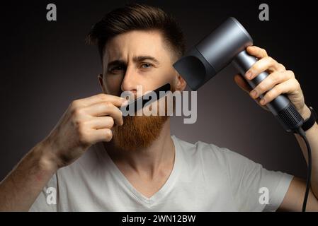 Un homme sèche sa barbe avec un sèche-cheveux Banque D'Images