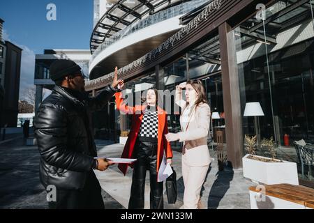 Trois jeunes se sont rassemblés dans un quartier d’affaires. On pointe vers le haut, gestuel et discutant sous le soleil urbain. Banque D'Images