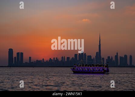 Une image colorée du centre-ville de Dubaï au coucher du soleil, avec un bateau de fête éclairé naviguant sur la crique de Dubaï. Banque D'Images