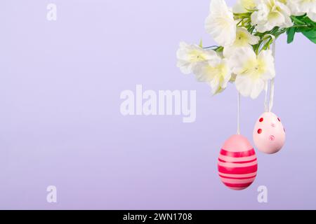 Deux beaux œufs de Pâques roses se balançant doucement d'une branche en herbe sur un fond violet tranquille Banque D'Images