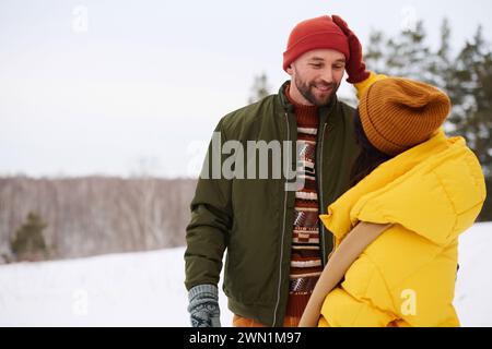 Jeune femme méconnaissable portant une veste gonflante debout à l'extérieur le jour d'hiver tapoter la tête de son mari, copier l'espace Banque D'Images