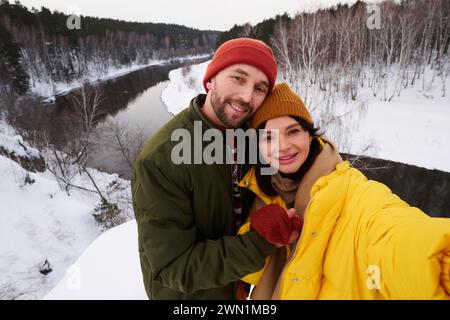 Joyeux homme caucasien et femme amoureux debout sur la falaise contre la rivière prenant selfie sur smartphone Banque D'Images