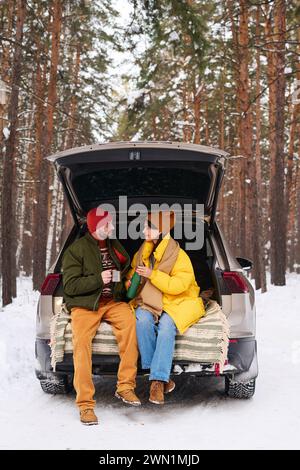 Jeune couple caucasien assis dans le coffre de voiture buvant du thé et parlant le froid jour d'hiver Banque D'Images