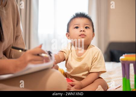 Un petit garçon asiatique mignon et innocent essaie de jouer et de déranger sa mère pendant qu'elle travaille à la maison. enfance, petit fils, enfant Banque D'Images