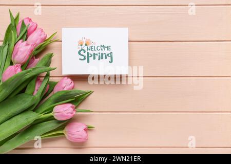 Carte de voeux avec texte de BIENVENUE PRINTEMPS et belles tulipes sur fond de bois rose Banque D'Images