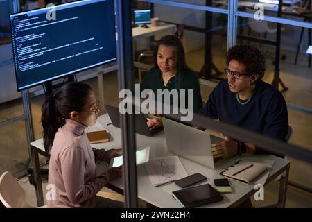 Vue sous un angle élevé d'ingénieurs ethniquement divers travaillant ensemble sur des logiciels dans les bureaux de l'entreprise INFORMATIQUE tard dans la soirée Banque D'Images