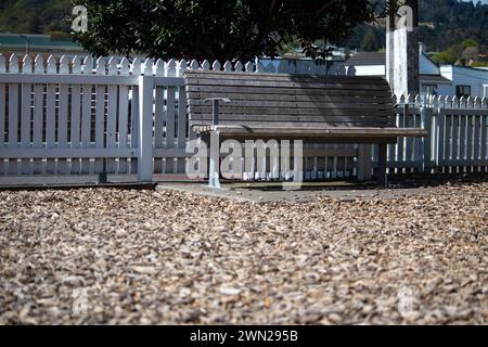 Un banc de parc unique dans une aire de jeux pour enfants, est inoccupé par une journée ensoleillée - abandonné, peu fréquenté, vacant et oublié. Banque D'Images