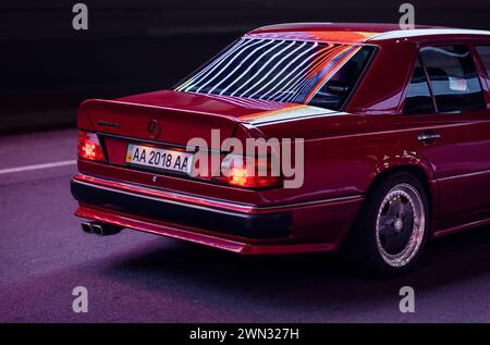 Vue de trois quarts arrière de Mercedes-Benz 400E (W124) dans le kit de carrosserie AMG la nuit. berline allemande des années 1980 reflétant les néons de rue. Banque D'Images